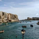 A small bay full of small wooden fishing boats, surrounded by tall apartment buildings. Spinola Bay has some of the best hotels in Malta.