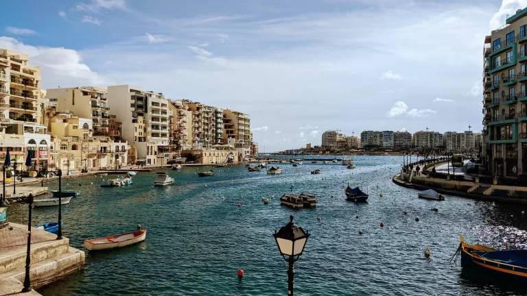 A small bay full of small wooden fishing boats, surrounded by tall apartment buildings. Spinola Bay has some of the best hotels in Malta.