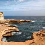 A small bay carved out of limestone rocks with deep blue sea splashing against the rocks