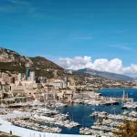 A sunny harbour with shining yachts and boats, with mountains and blue skies in the background