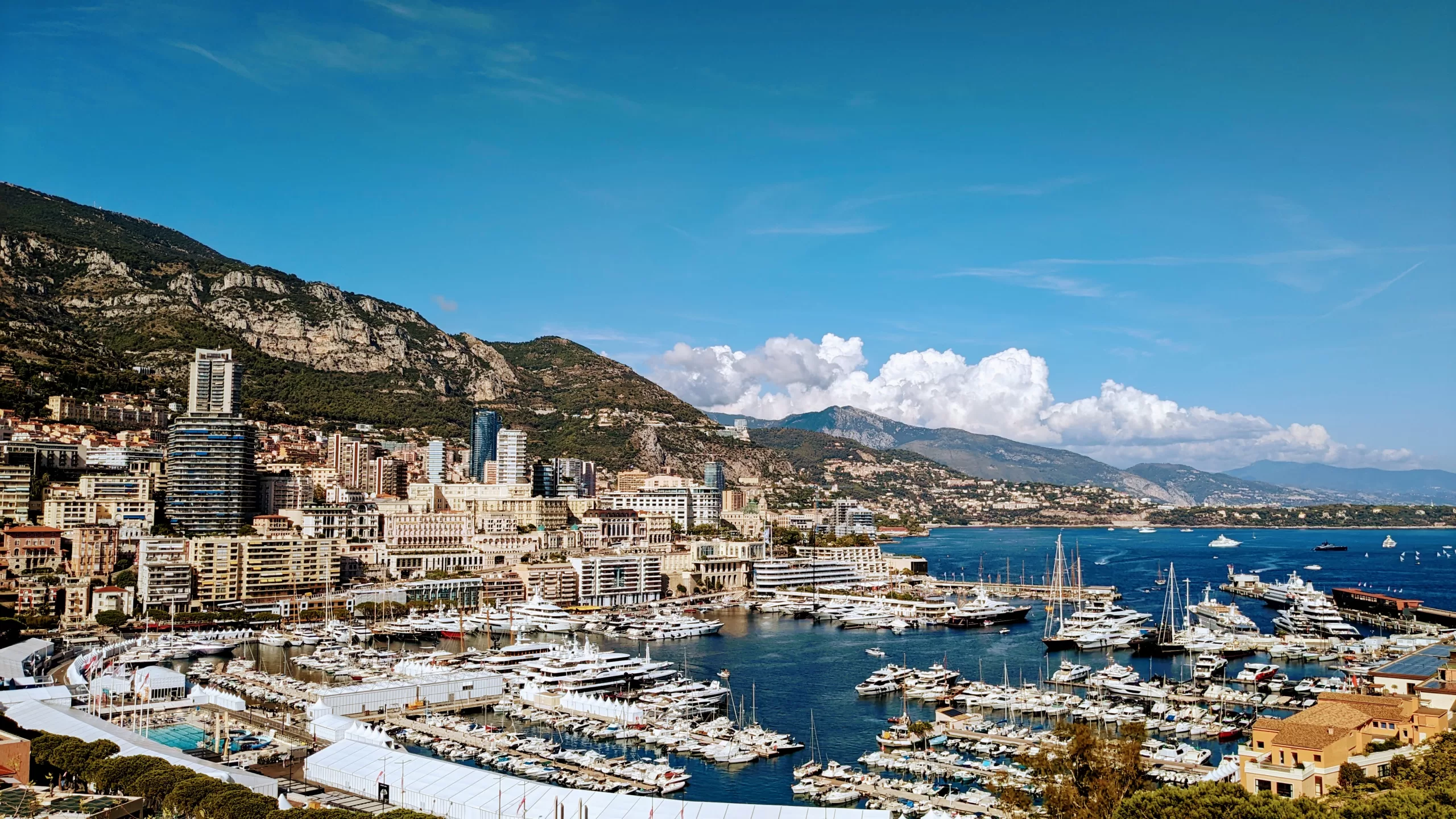 A sunny harbour with shining yachts and boats, with mountains and blue skies in the background