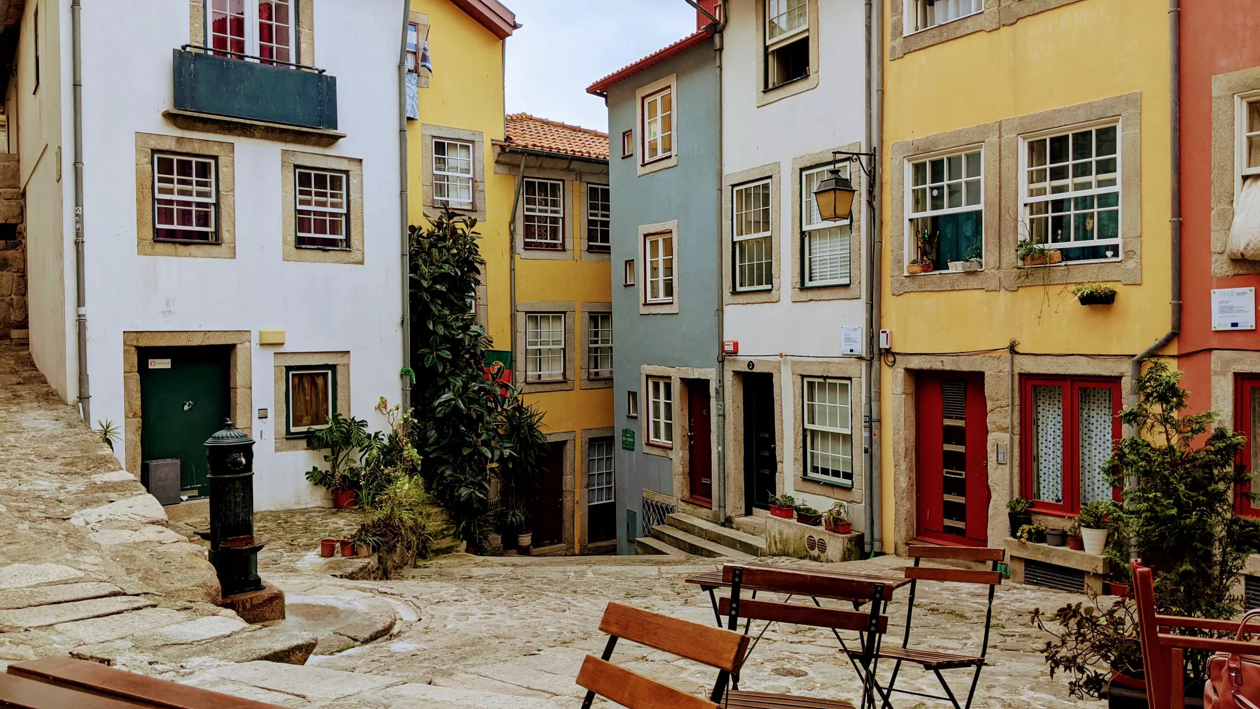 Colourful Portuguese alleyway with pastel-painted houses, cobblestone streets, small outdoor seating, and charming potted plants, ideal for travel photography and exploring Porto's vibrant neighbourhoods.