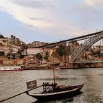 Vibrant riverfront view of Porto, Portugal with colourful buildings and iconic Dom Luís I Bridge at sunset.