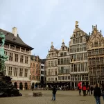 Elaborate on the cityscape of Antwerp with historic medieval buildings and a prominent statue in a lively square.