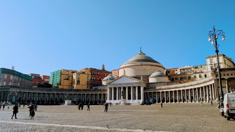 A white church is flanked by colonnades, opening up round a white marble square.