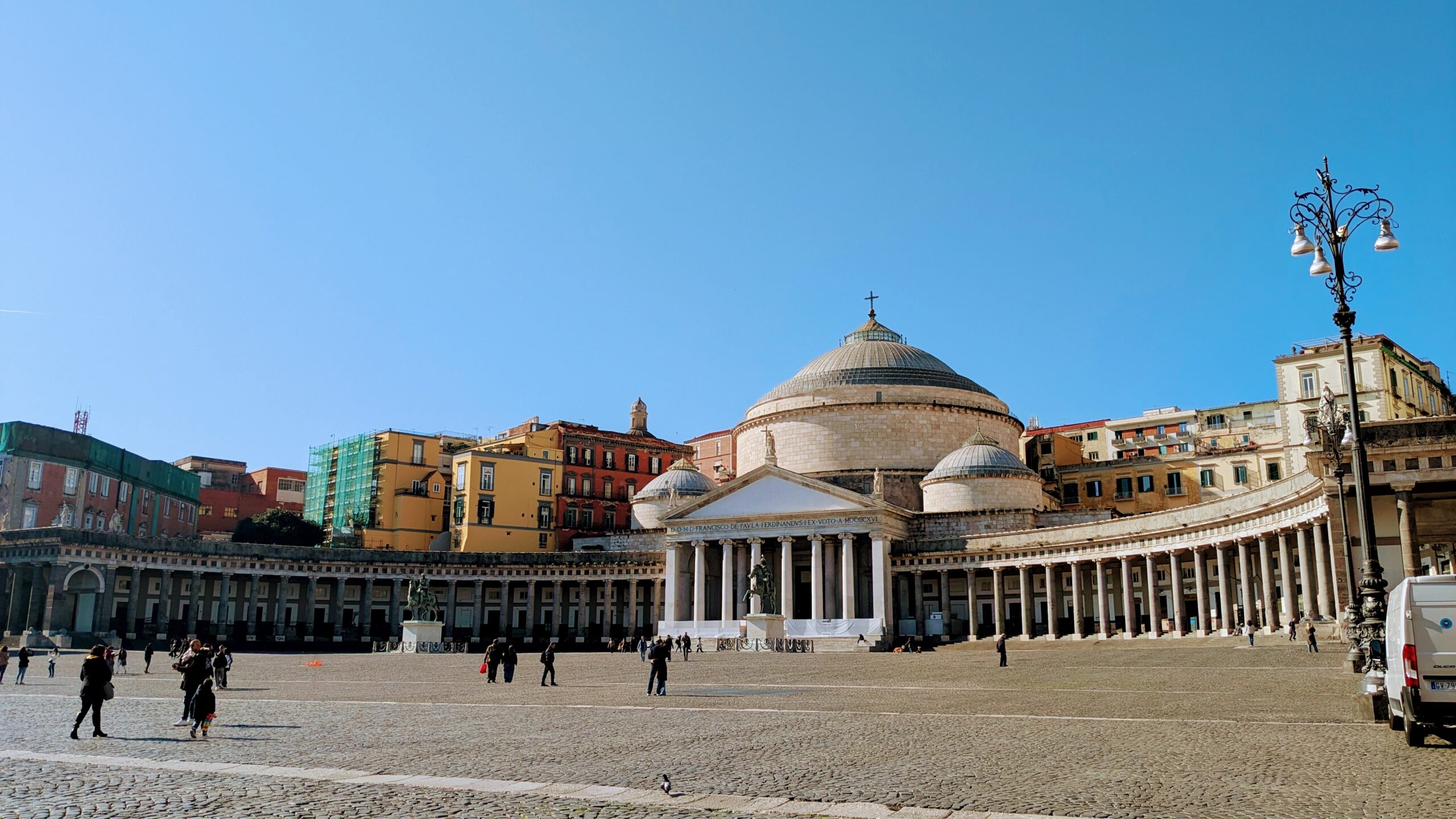 A white church is flanked by colonnades, opening up round a white marble square.