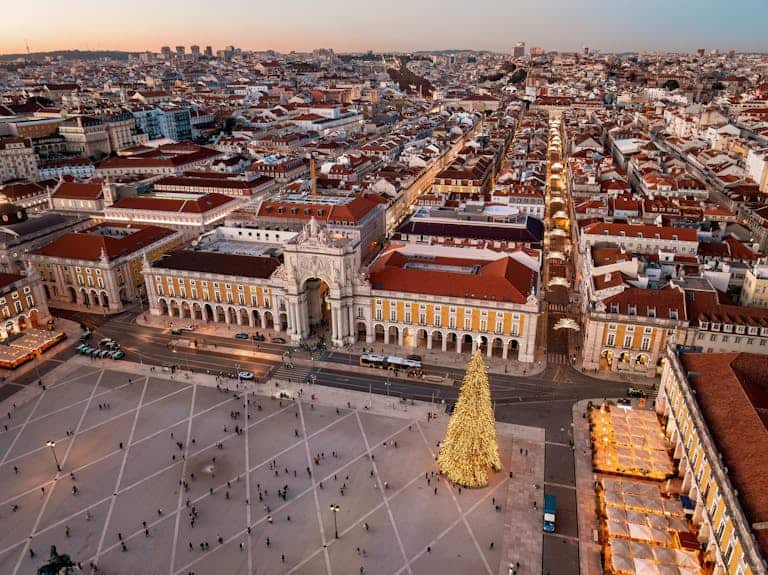A stunning aerial view of Lisbon's cityscape with a festive Christmas tree in Praça do Comércio at sunset.