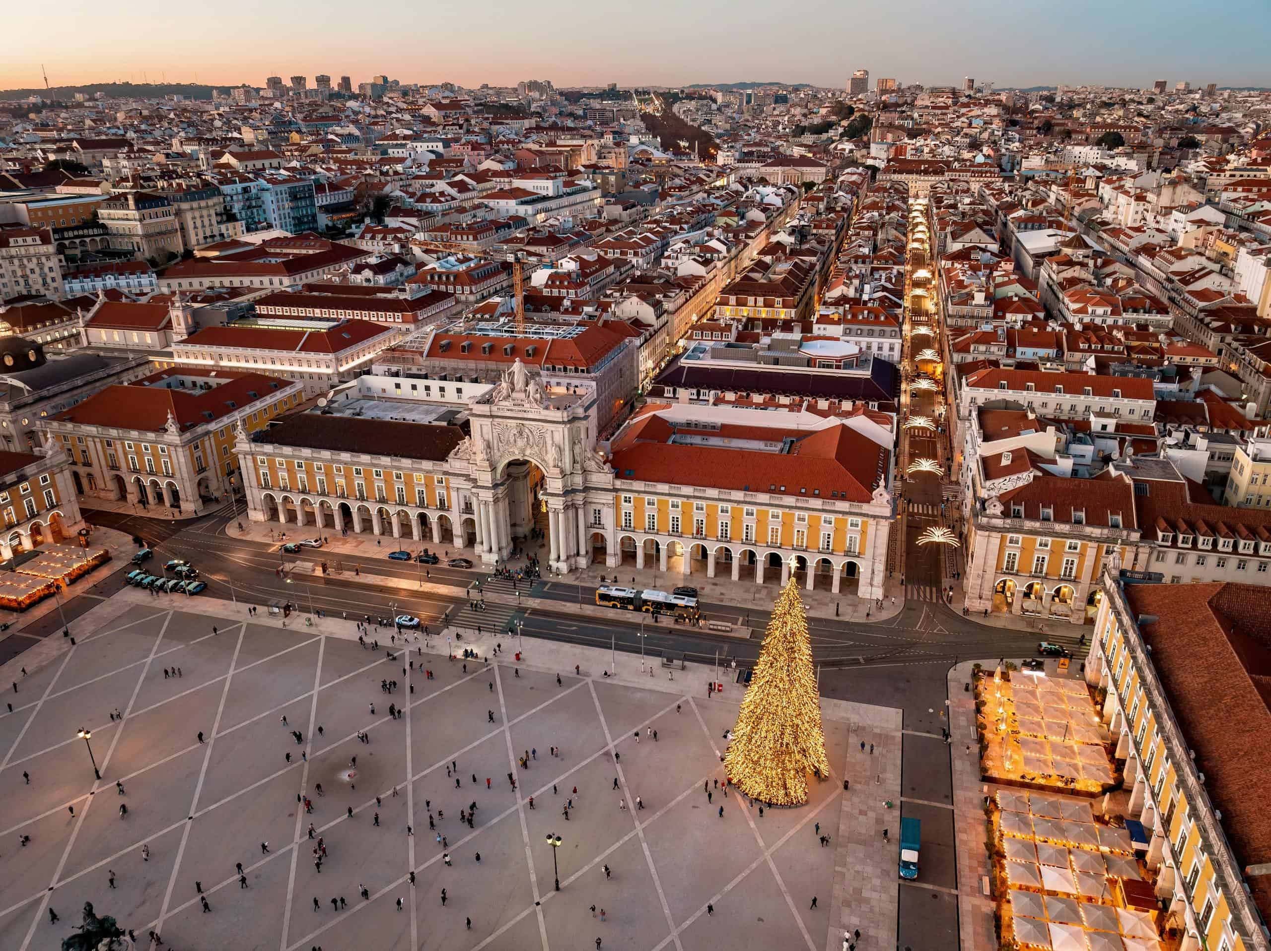 A stunning aerial view of Lisbon's cityscape with a festive Christmas tree in Praça do Comércio at sunset.