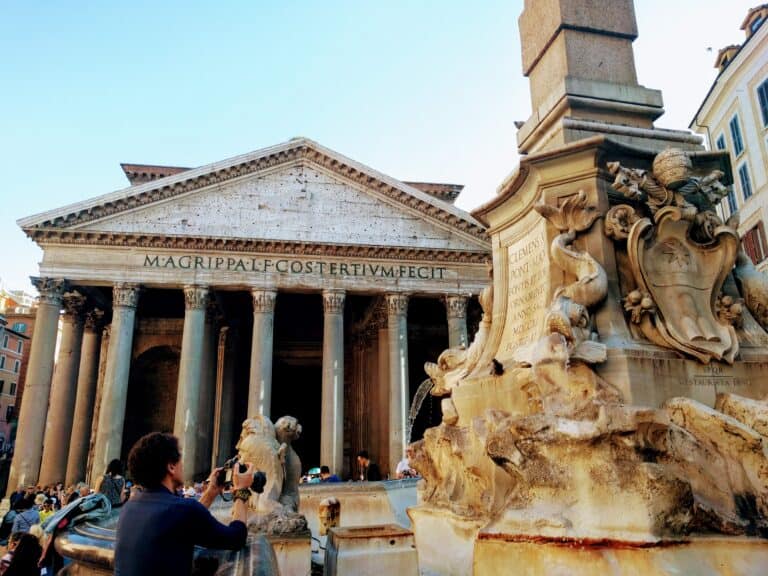 The white stone pantheon rises up behind an ornate stone waterfall, with some tourists in between them