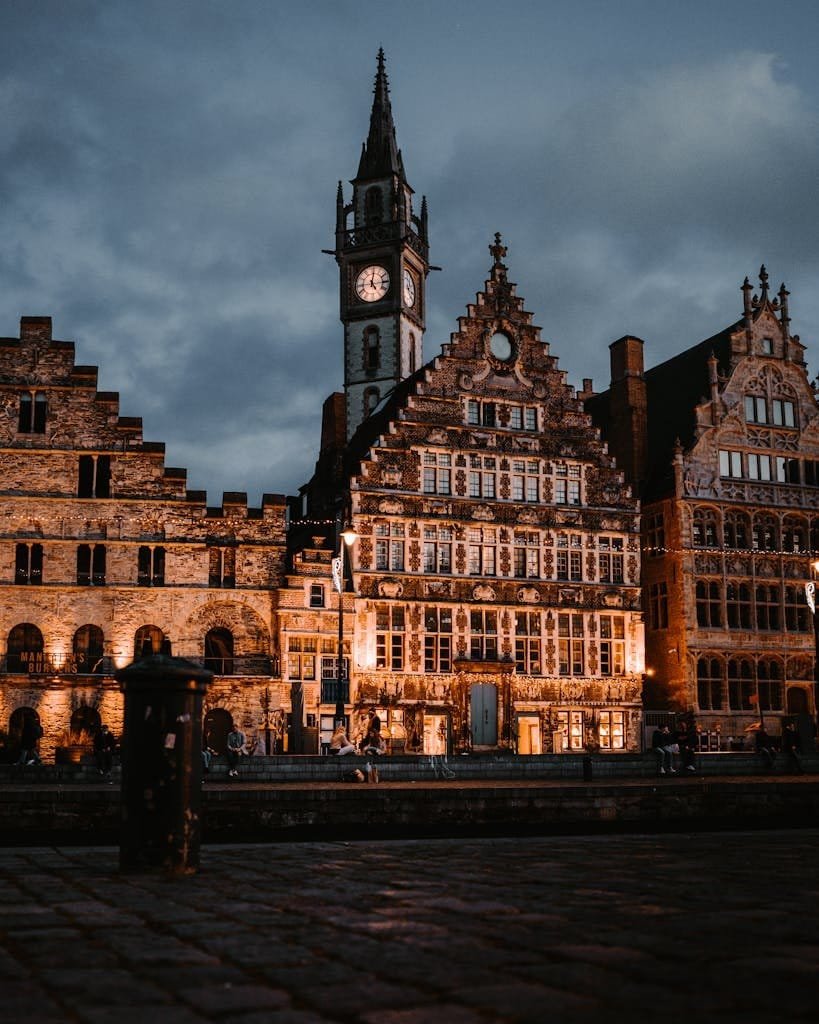 Illuminated medieval architecture and clock tower in Ghent, Belgium at night.