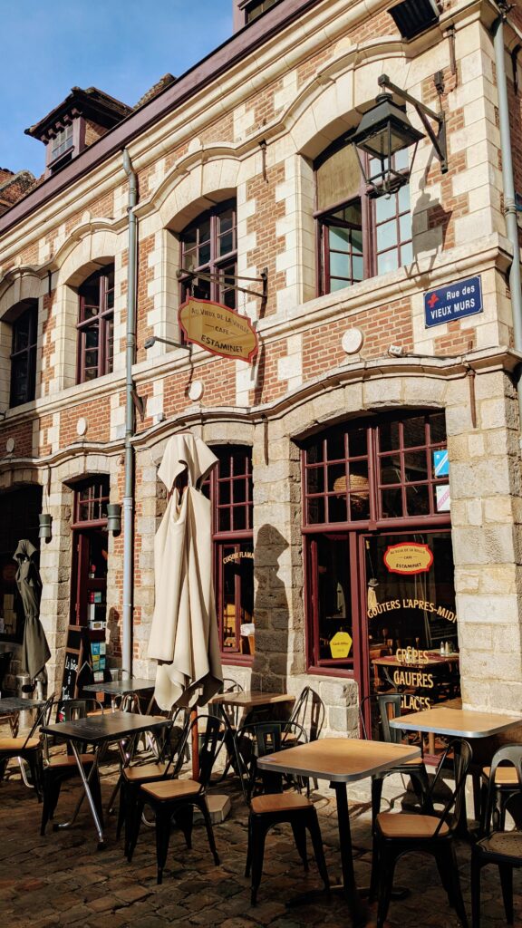 Quaint Parisian café on a cobbled street with outdoor seating, traditional architecture, and charming signage, perfect for experiencing local French culture and enjoying delicious pastries and coffee.