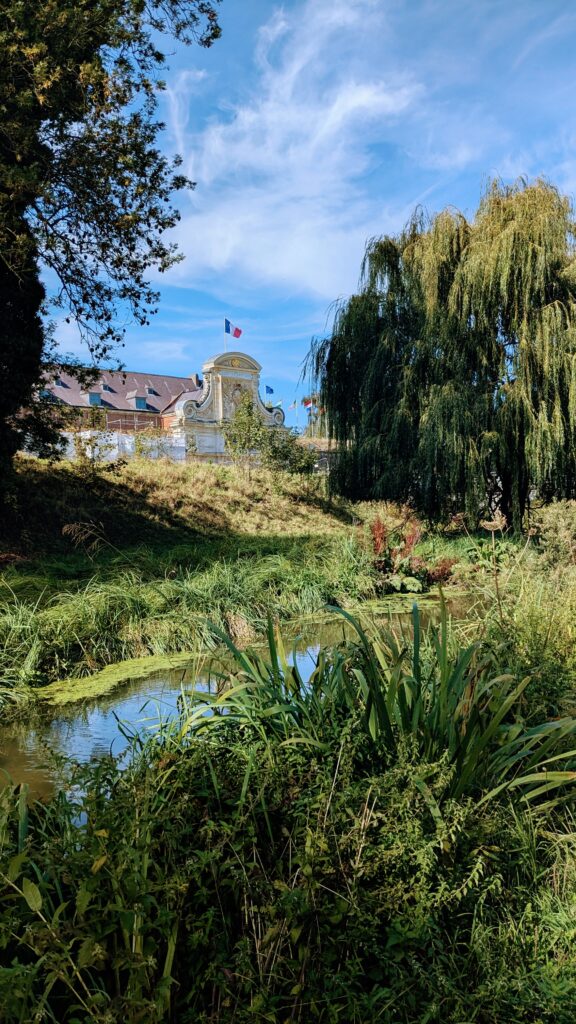 Lush riverside greenery with a historic building and flags in the background, showcasing picturesque outdoor scenery in a travel destination.