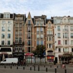 Charming Parisian buildings with classic architecture line a bustling street scene, featuring cafes, shops, and pedestrians, capturing the essence of a vibrant Paris neighbourhood for travel enthusiasts.