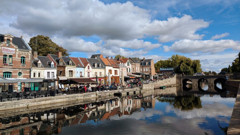 Charming riverside town in France with colourful historic buildings, outdoor cafes, and a stone bridge reflected in the calm water, showcasing picturesque European cityscape and leisurely outdoor lifestyle.
