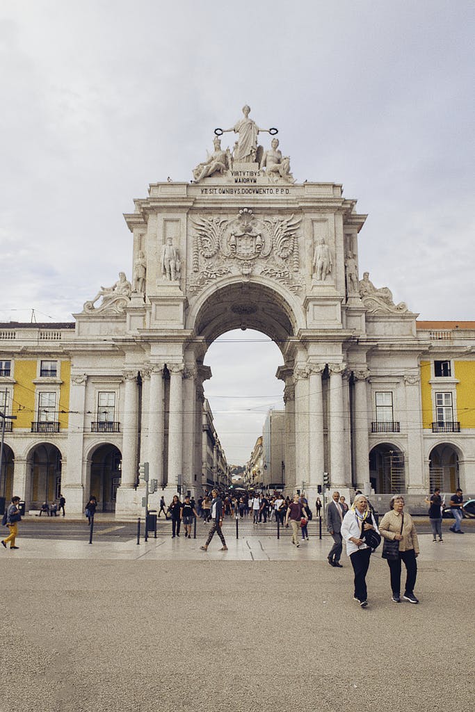 Elegant historic triumphal arch in Lisbon Portugal, adorned with sculptures and inscriptions, busy with tourists and locals, showcasing Portuguese architecture and culture.
