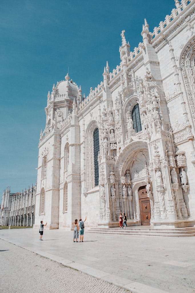 Majestic white castle in Portugal with intricate gothic architecture and visitors exploring in sunny weather.