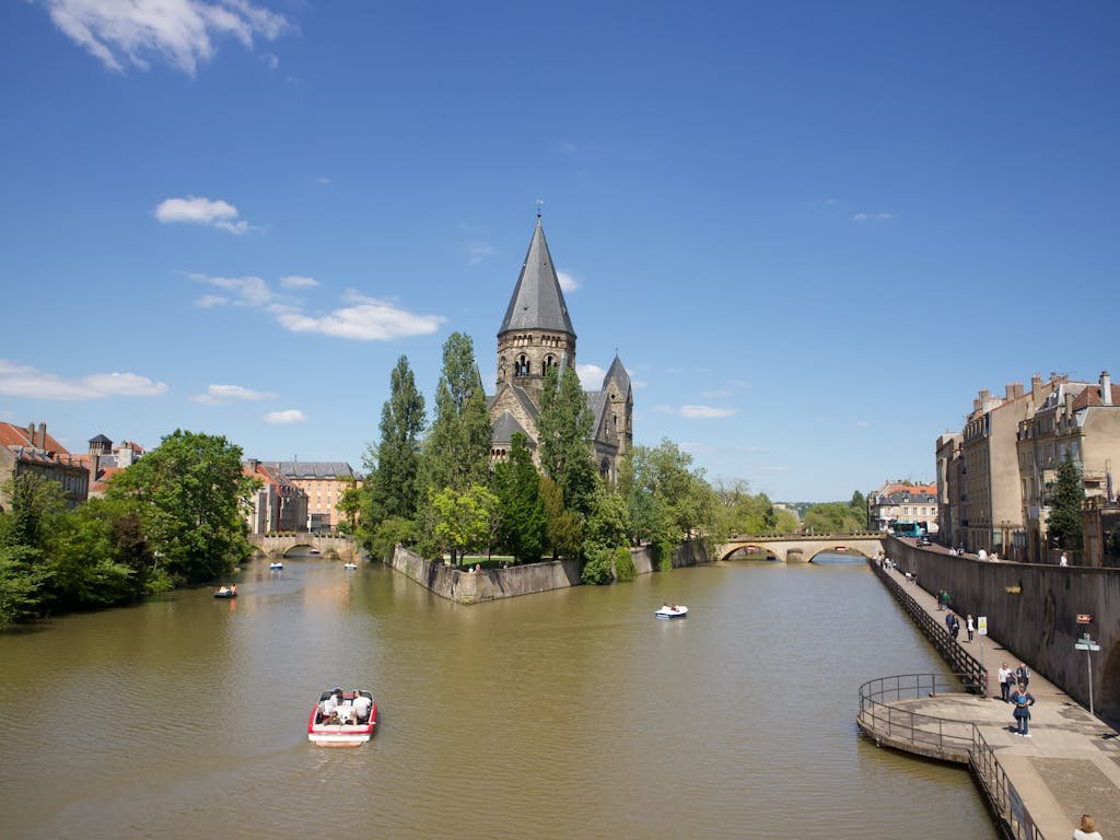 Historic church on riverbank in scenic cityscape, vibrant blue sky, boating and walking in a popular European travel destination, ideal for cultural exploration and outdoor activities.
