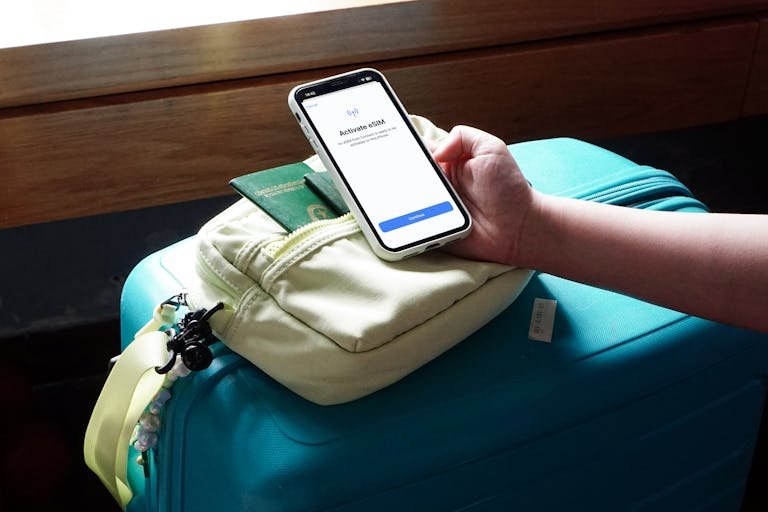 Close-up of a traveler activating eSIM on a smartphone over luggage, ready for a trip.