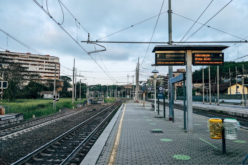 Serene view of an empty Rome train station platform with tracks and urban backdrop at dawn.