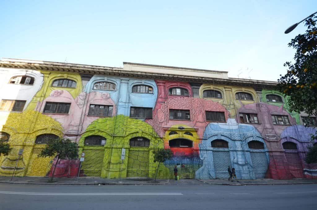 Vibrant street art featuring abstract faces and bold colours on a historic building in Rome, perfect for exploring off-the-beaten-path locations in the city. Ostiense is a great option if you don't know where to stay in Rome.